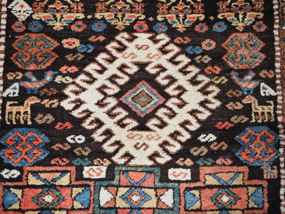 An antique Kurdish wool runner rug featuring a dark central field filled with diamond latch hook medallions and geometric polychrome borders. View XI