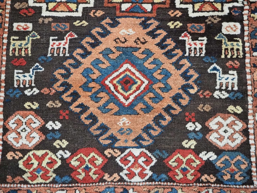 An antique Kurdish wool runner rug featuring a dark central field filled with diamond latch hook medallions and geometric polychrome borders. View XII