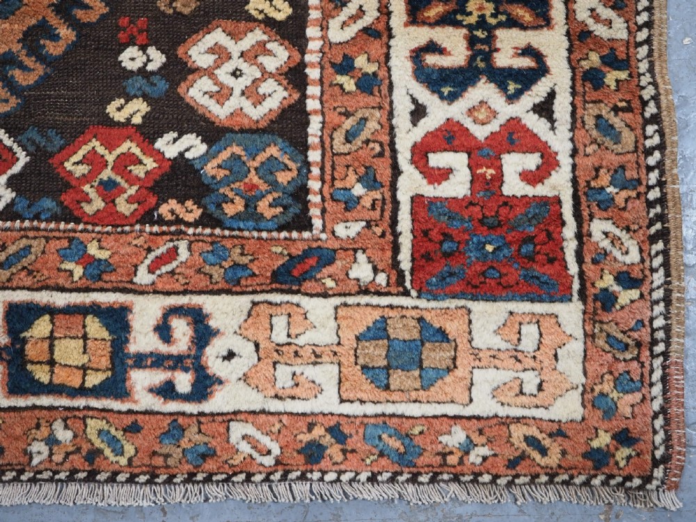 An antique Kurdish wool runner rug featuring a dark central field filled with diamond latch hook medallions and geometric polychrome borders. View XIII