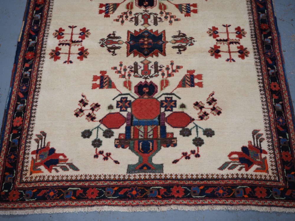 A hand-woven antique Afshar wool rug featuring geometric vase motifs in red, navy, and green on an ivory field with a dark border. View V