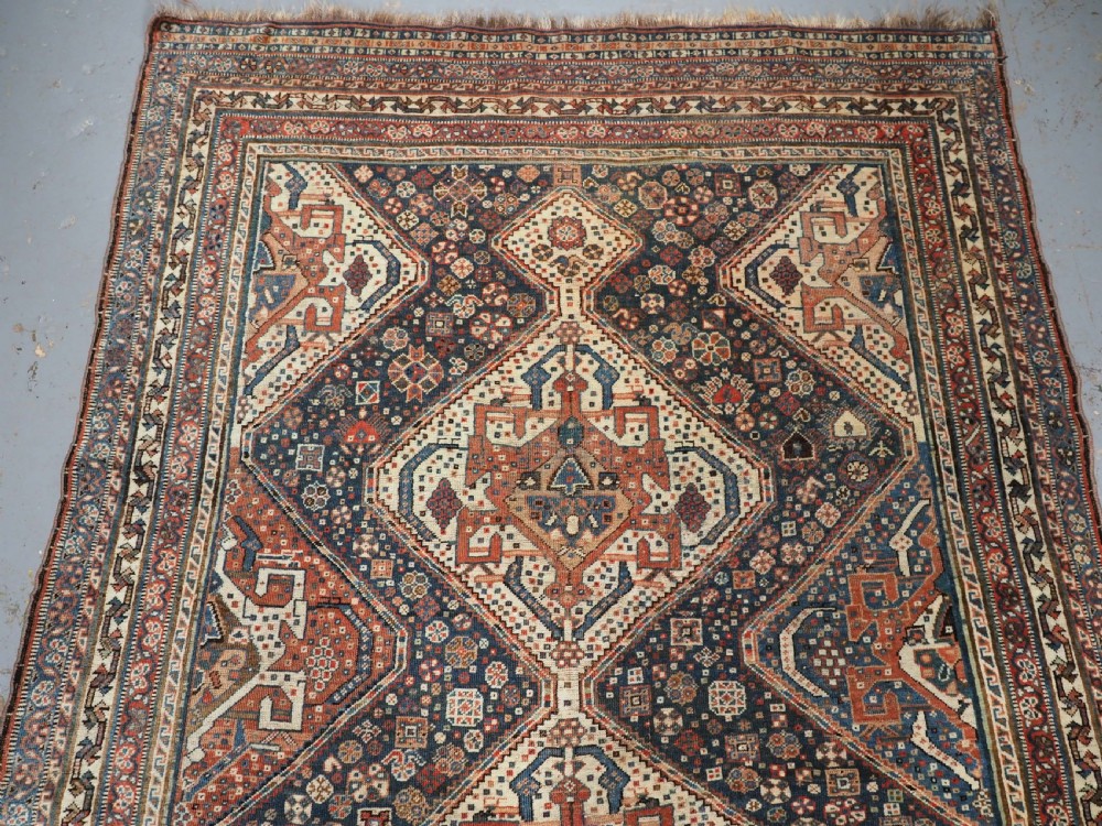 An antique rectangular wool rug featuring three diamond-shaped medallions along a central dark blue field surrounded by geometric borders in terracotta, cream, and blue tones. View III