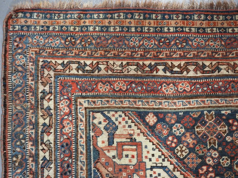 An antique rectangular wool rug featuring three diamond-shaped medallions along a central dark blue field surrounded by geometric borders in terracotta, cream, and blue tones. View VII