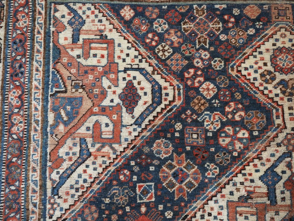 An antique rectangular wool rug featuring three diamond-shaped medallions along a central dark blue field surrounded by geometric borders in terracotta, cream, and blue tones. View XI