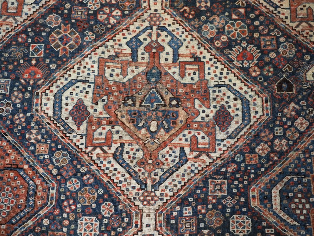 An antique rectangular wool rug featuring three diamond-shaped medallions along a central dark blue field surrounded by geometric borders in terracotta, cream, and blue tones. View XII