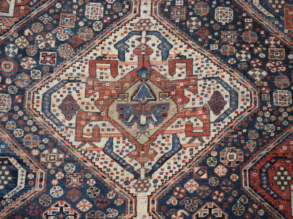 An antique rectangular wool rug featuring three diamond-shaped medallions along a central dark blue field surrounded by geometric borders in terracotta, cream, and blue tones. View XIII