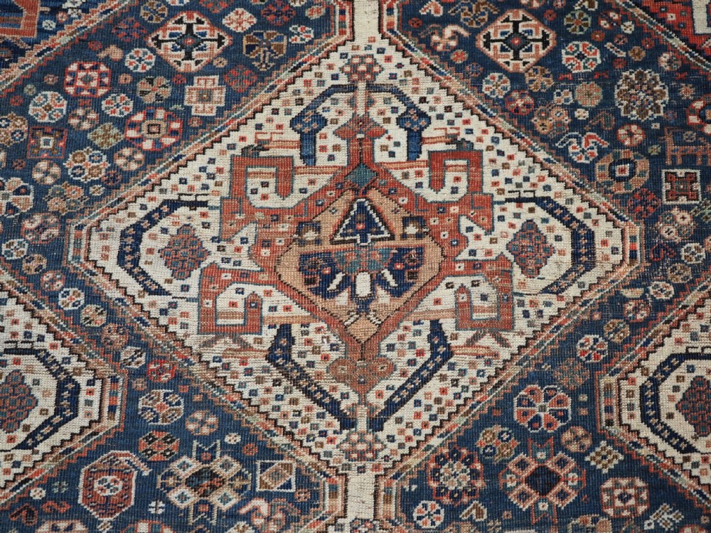 An antique rectangular wool rug featuring three diamond-shaped medallions along a central dark blue field surrounded by geometric borders in terracotta, cream, and blue tones. View XIV