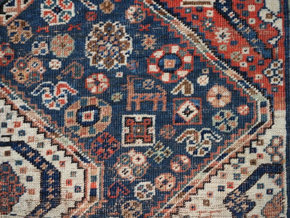 An antique rectangular wool rug featuring three diamond-shaped medallions along a central dark blue field surrounded by geometric borders in terracotta, cream, and blue tones. View XV