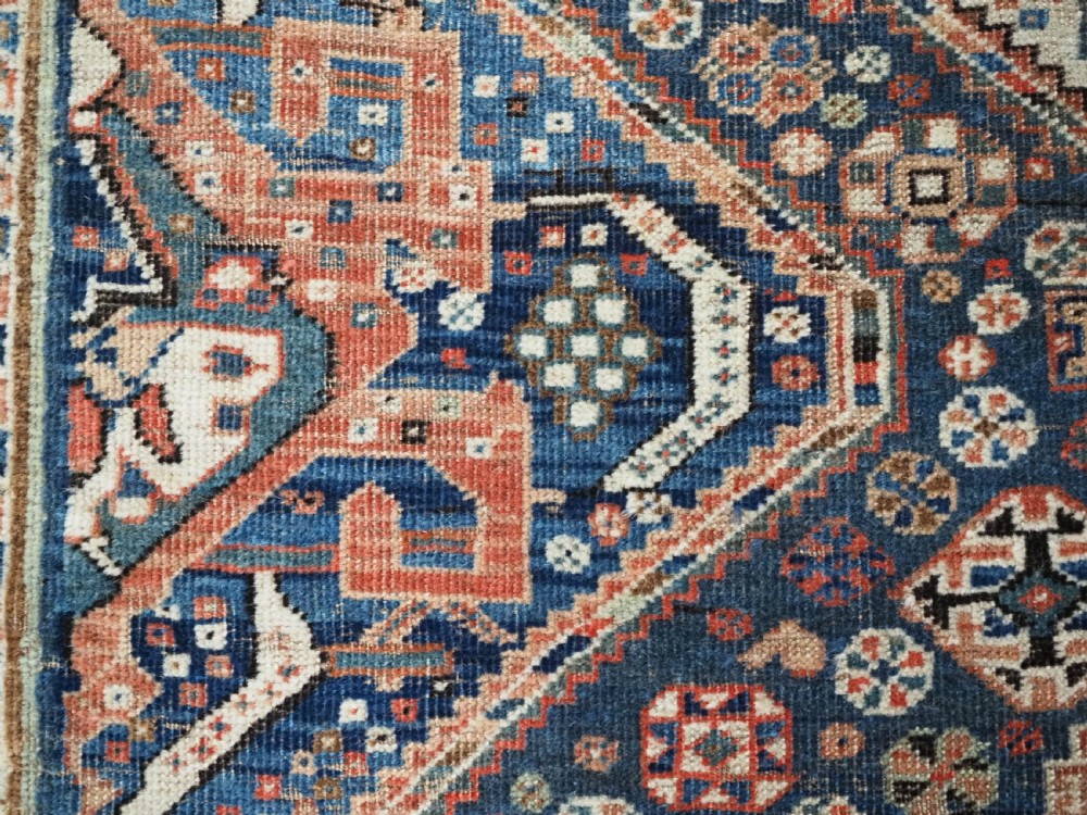 An antique rectangular wool rug featuring three diamond-shaped medallions along a central dark blue field surrounded by geometric borders in terracotta, cream, and blue tones. View XVI