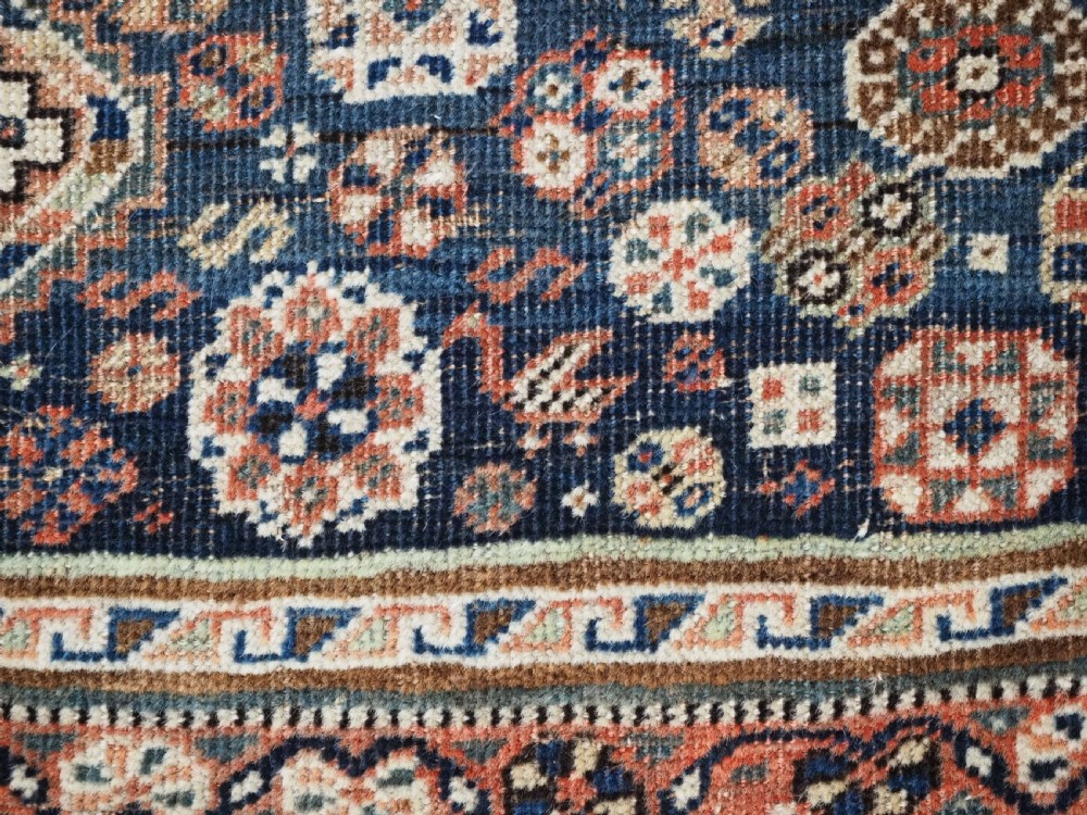 An antique rectangular wool rug featuring three diamond-shaped medallions along a central dark blue field surrounded by geometric borders in terracotta, cream, and blue tones. View XVII