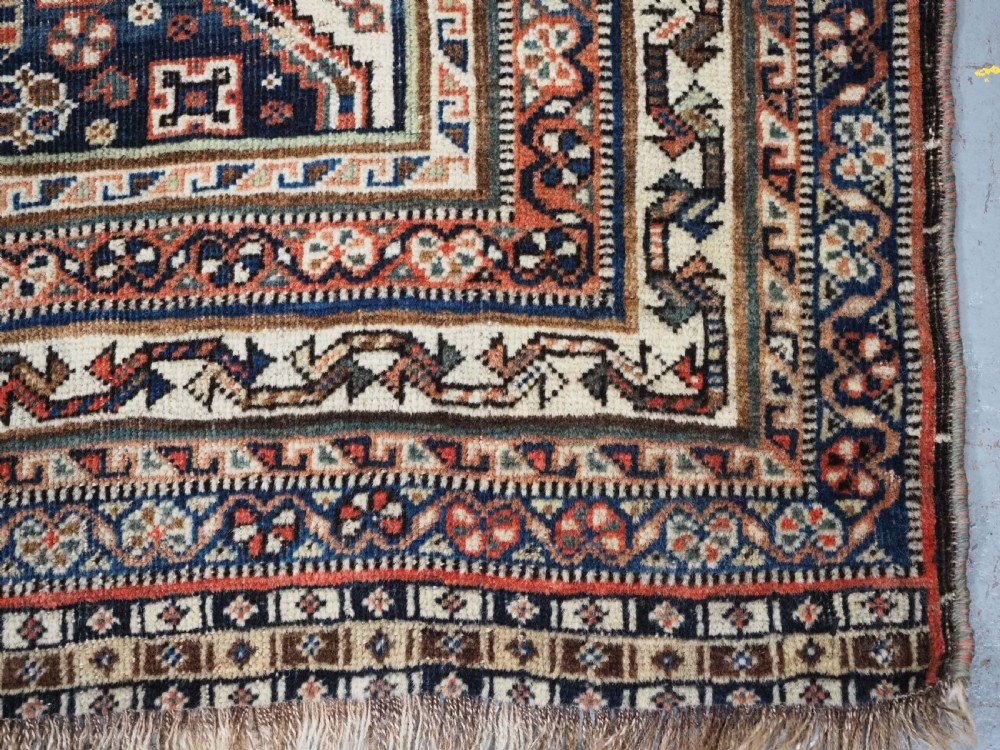 An antique rectangular wool rug featuring three diamond-shaped medallions along a central dark blue field surrounded by geometric borders in terracotta, cream, and blue tones. View XVIII