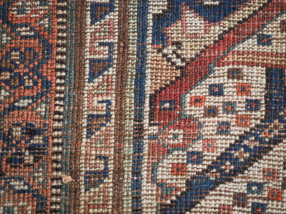 An antique rectangular wool rug featuring three diamond-shaped medallions along a central dark blue field surrounded by geometric borders in terracotta, cream, and blue tones. View XIX