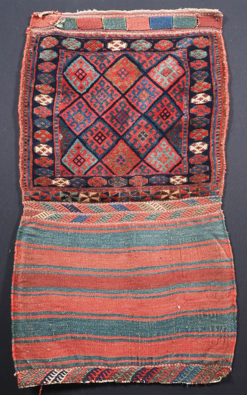 An antique Kurdish Jaf tribal bag featuring a hand-knotted diamond geometric pattern on the front and a striped plain weave backing in red, blue, and teal shades.
