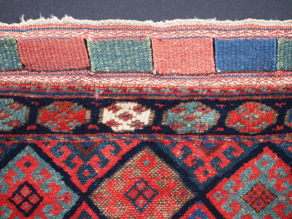 An antique Kurdish Jaf tribal bag featuring a hand-knotted diamond geometric pattern on the front and a striped plain weave backing in red, blue, and teal shades. View V