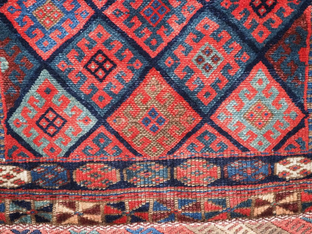 An antique Kurdish Jaf tribal bag featuring a hand-knotted diamond geometric pattern on the front and a striped plain weave backing in red, blue, and teal shades. View VI