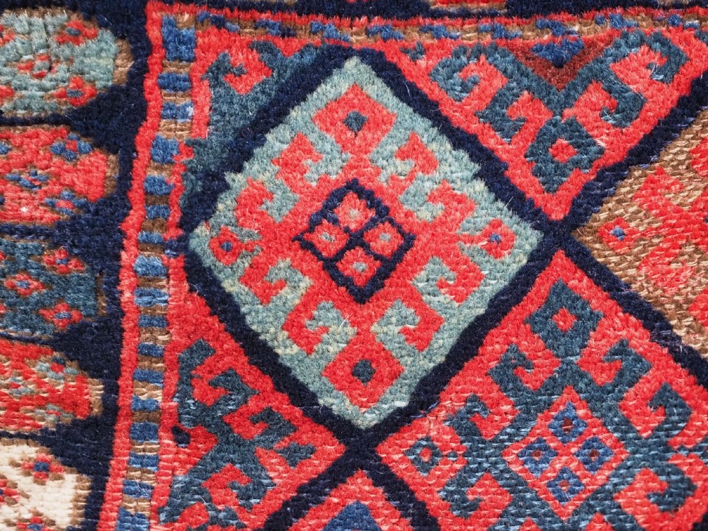 An antique Kurdish Jaf tribal bag featuring a hand-knotted diamond geometric pattern on the front and a striped plain weave backing in red, blue, and teal shades. View VII