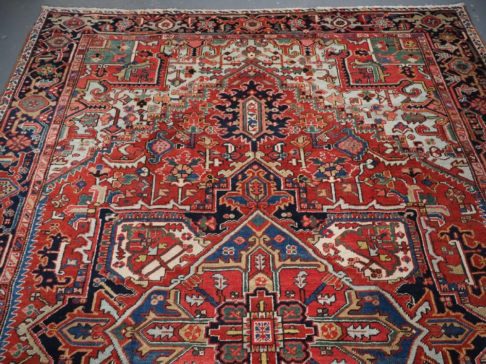 An antique hand-knotted Heriz wool carpet featuring a large geometric central medallion in navy blue, rust red, and cream on a patterned field. View III