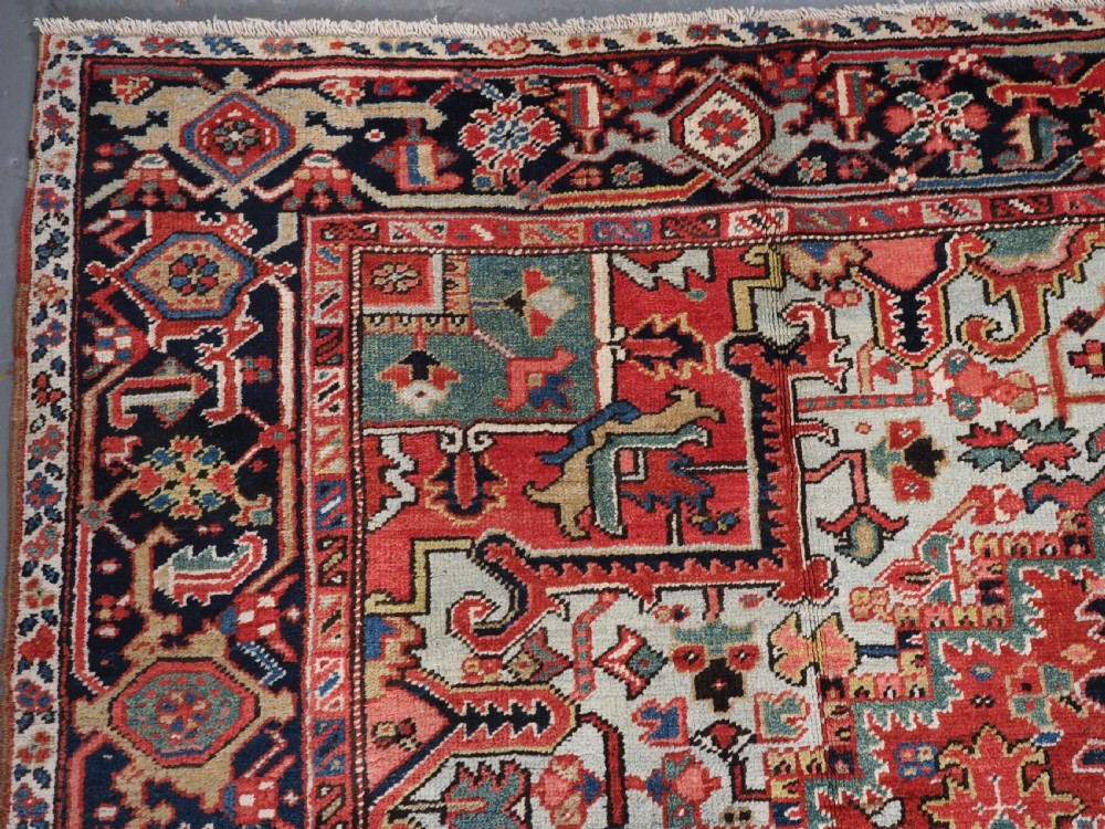 An antique hand-knotted Heriz wool carpet featuring a large geometric central medallion in navy blue, rust red, and cream on a patterned field. View VI
