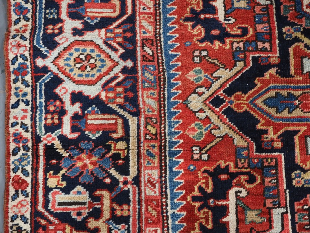 An antique hand-knotted Heriz wool carpet featuring a large geometric central medallion in navy blue, rust red, and cream on a patterned field. View VII