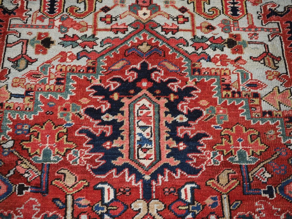 An antique hand-knotted Heriz wool carpet featuring a large geometric central medallion in navy blue, rust red, and cream on a patterned field. View VIII