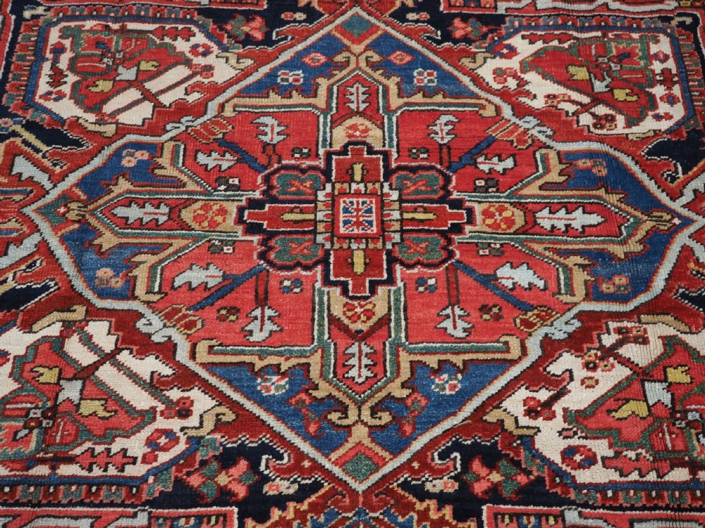 An antique hand-knotted Heriz wool carpet featuring a large geometric central medallion in navy blue, rust red, and cream on a patterned field. View IX