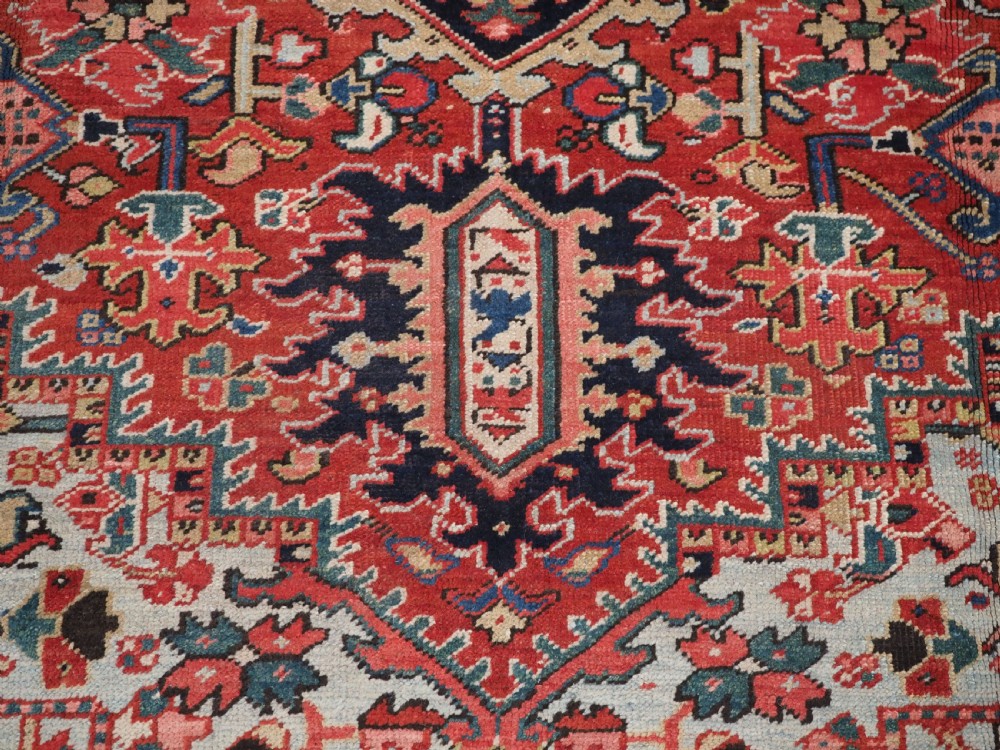 An antique hand-knotted Heriz wool carpet featuring a large geometric central medallion in navy blue, rust red, and cream on a patterned field. View X