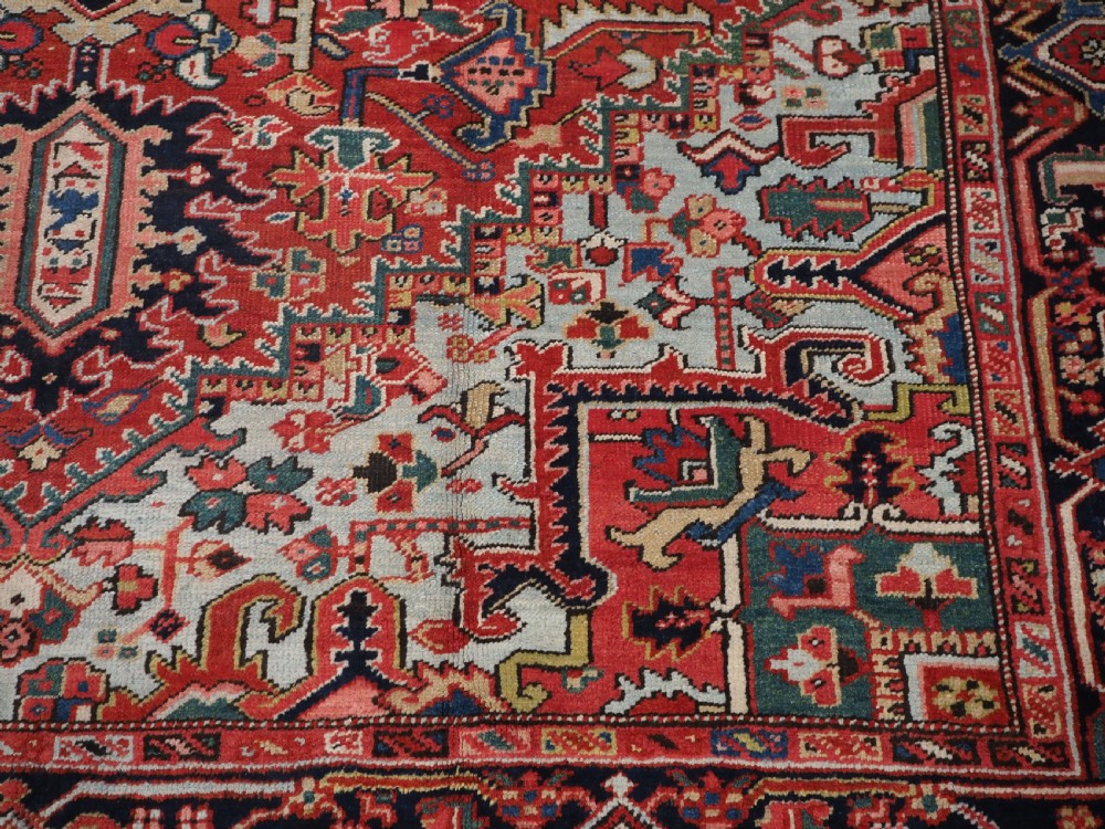 An antique hand-knotted Heriz wool carpet featuring a large geometric central medallion in navy blue, rust red, and cream on a patterned field. View XI