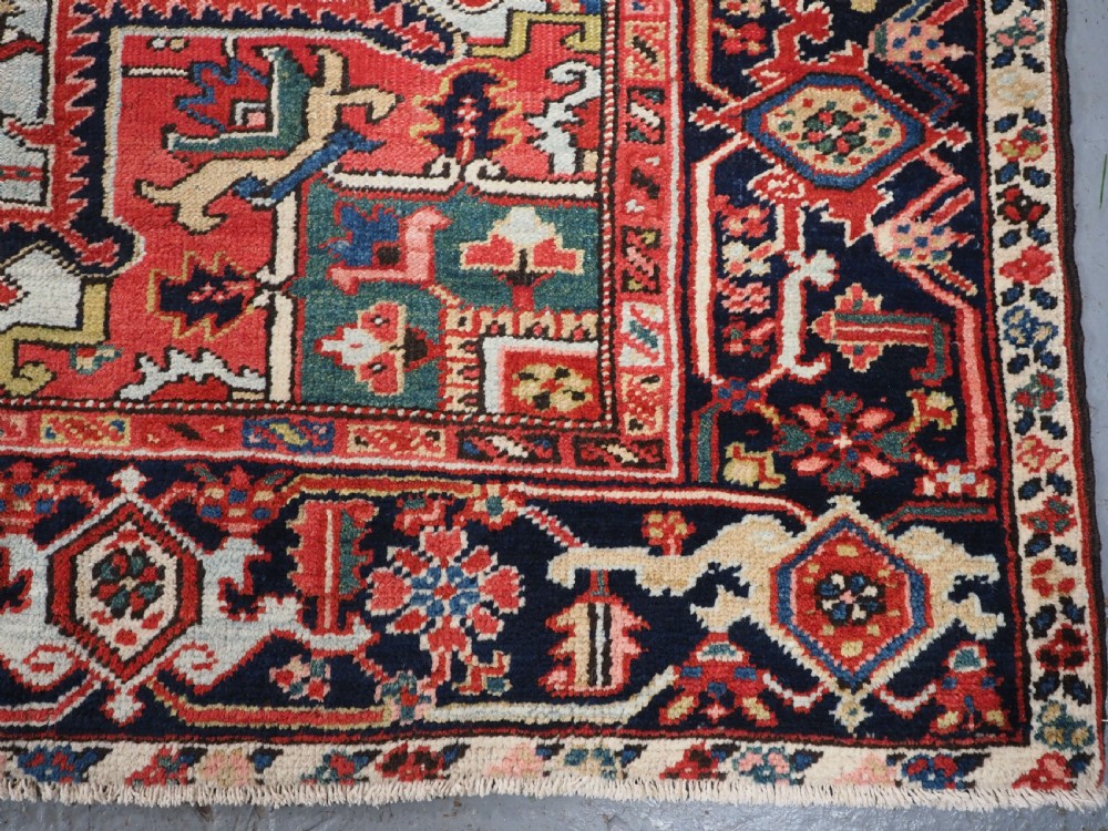 An antique hand-knotted Heriz wool carpet featuring a large geometric central medallion in navy blue, rust red, and cream on a patterned field. View XII