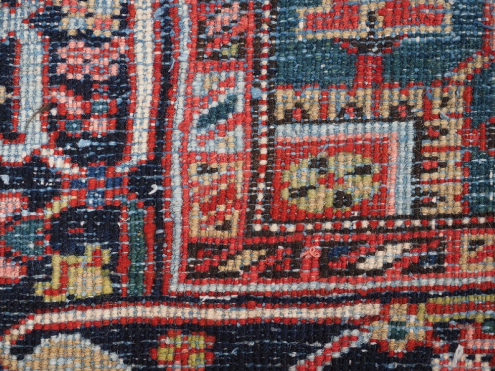 An antique hand-knotted Heriz wool carpet featuring a large geometric central medallion in navy blue, rust red, and cream on a patterned field. View XIII