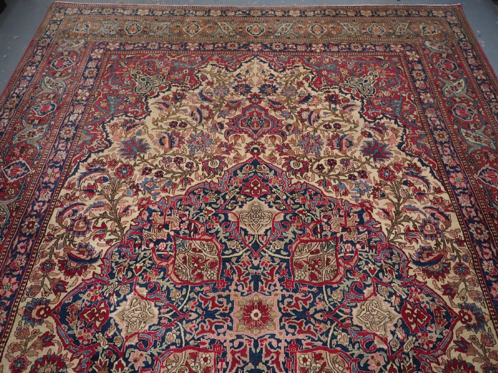 An antique rectangular Isfahan carpet featuring a detailed central medallion, cream field with red and blue floral arabesques, and a decorative multi-banded border. View III