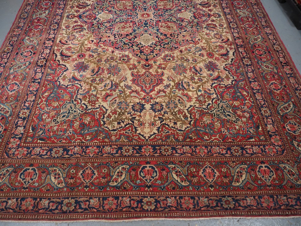 An antique rectangular Isfahan carpet featuring a detailed central medallion, cream field with red and blue floral arabesques, and a decorative multi-banded border. View V