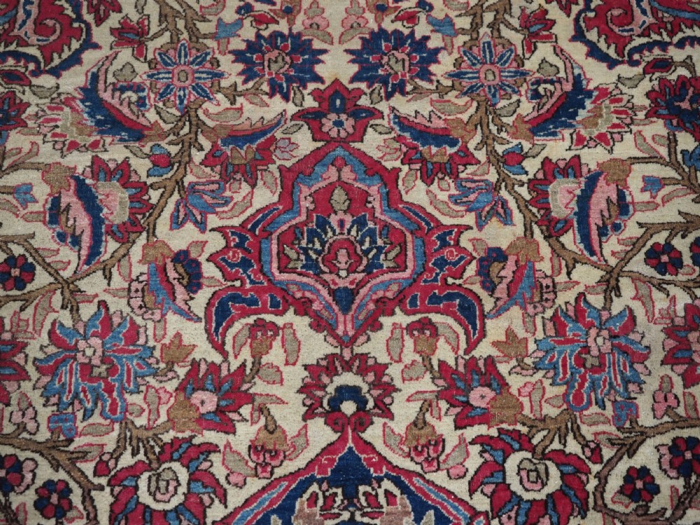 An antique rectangular Isfahan carpet featuring a detailed central medallion, cream field with red and blue floral arabesques, and a decorative multi-banded border. View IX