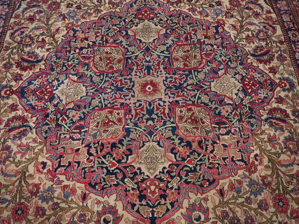 An antique rectangular Isfahan carpet featuring a detailed central medallion, cream field with red and blue floral arabesques, and a decorative multi-banded border. View X