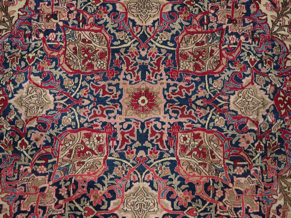 An antique rectangular Isfahan carpet featuring a detailed central medallion, cream field with red and blue floral arabesques, and a decorative multi-banded border. View XI