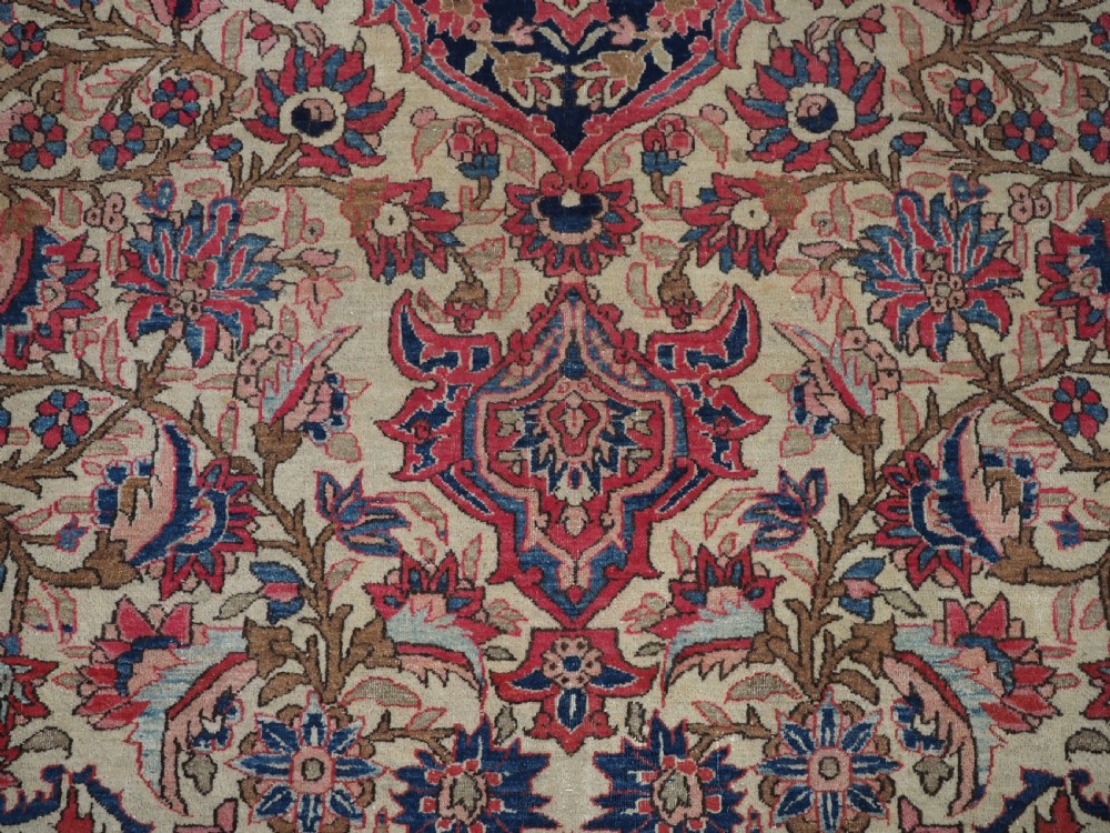An antique rectangular Isfahan carpet featuring a detailed central medallion, cream field with red and blue floral arabesques, and a decorative multi-banded border. View XII