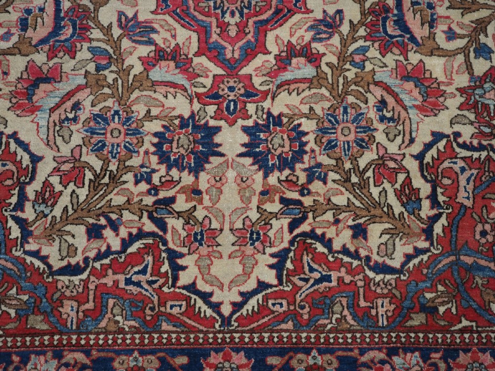 An antique rectangular Isfahan carpet featuring a detailed central medallion, cream field with red and blue floral arabesques, and a decorative multi-banded border. View XIV