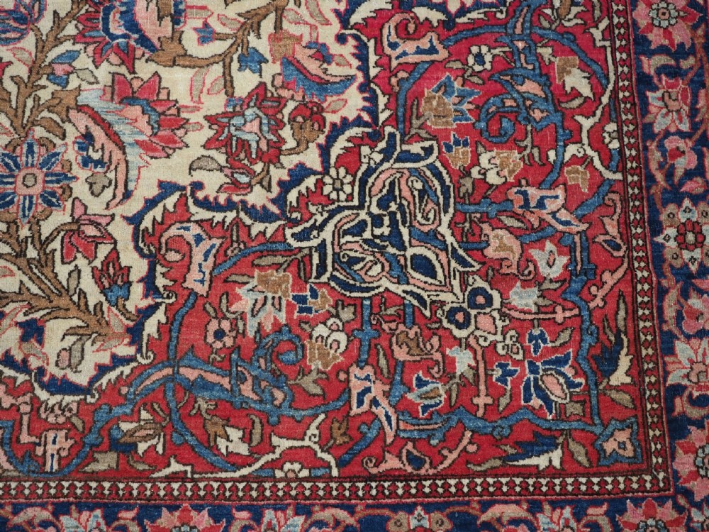 An antique rectangular Isfahan carpet featuring a detailed central medallion, cream field with red and blue floral arabesques, and a decorative multi-banded border. View XV