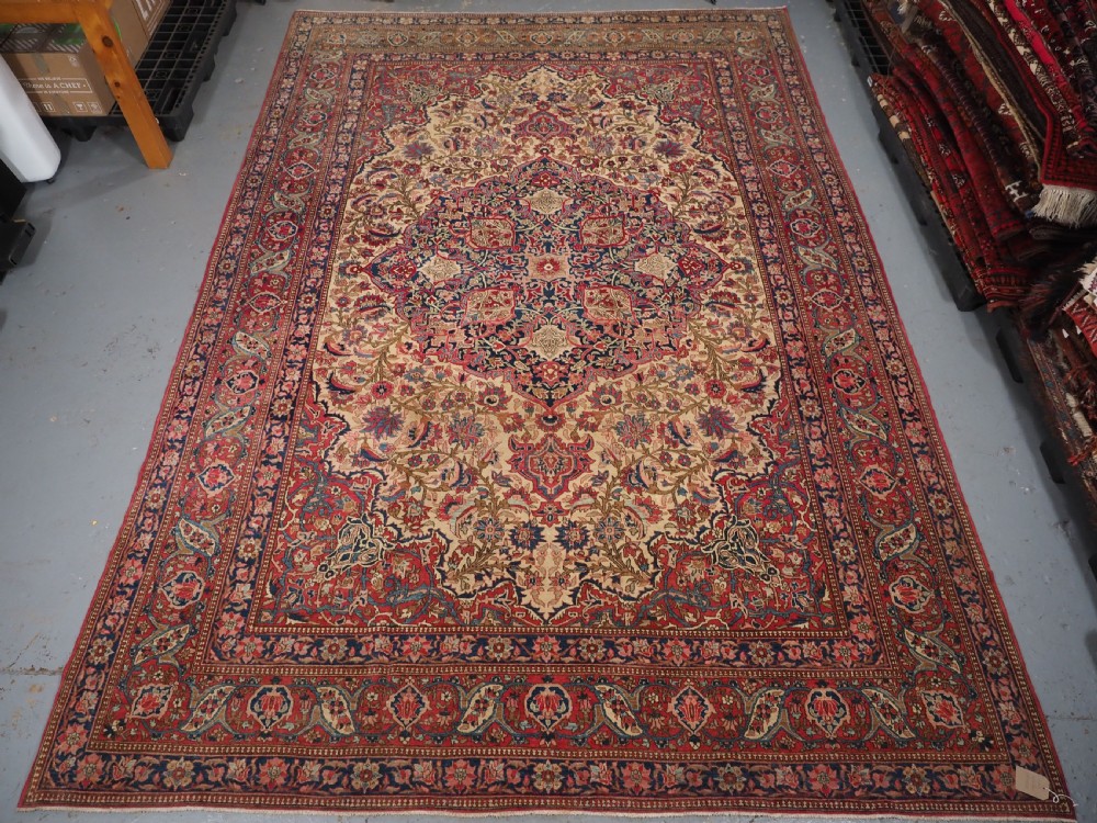 An antique rectangular Isfahan carpet featuring a detailed central medallion, cream field with red and blue floral arabesques, and a decorative multi-banded border. View XVIII