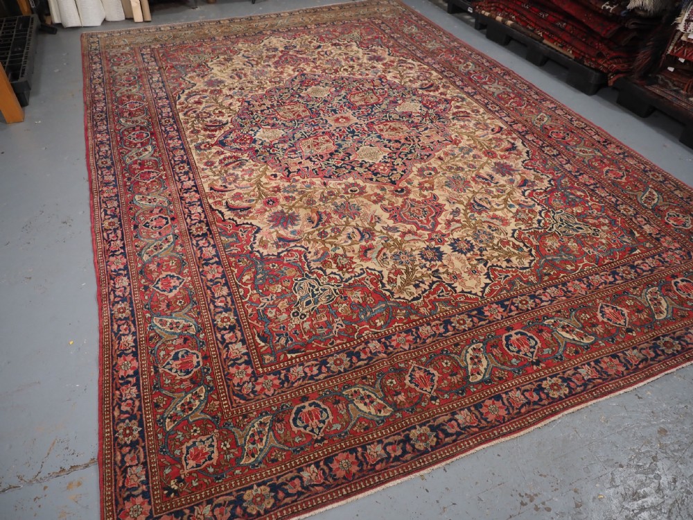 An antique rectangular Isfahan carpet featuring a detailed central medallion, cream field with red and blue floral arabesques, and a decorative multi-banded border. View XIX