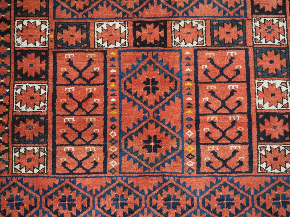 An antique rectangular hand-knotted wool Ersari Turkmen ensi rug featuring a four-panel hatchli pattern in terracotta red, dark blue, and ivory geometric motifs. View X