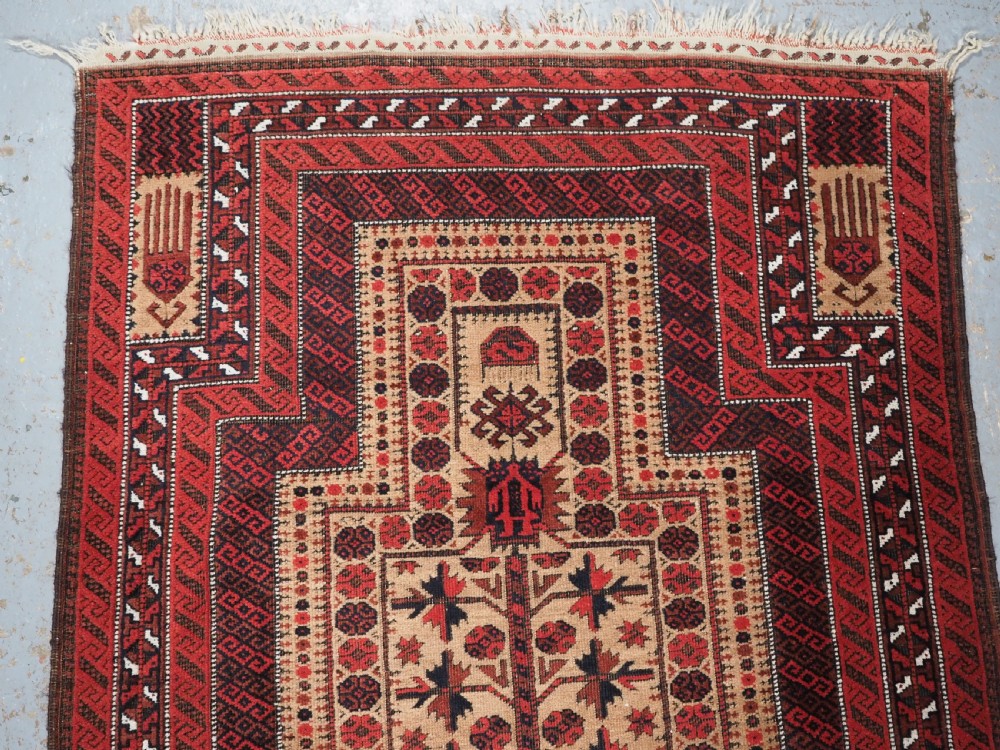 An antique Baluch wool prayer rug featuring a central mihrab arch, tree motifs, hand icons, and geometric borders in dark red, brown, and camel shades. View III