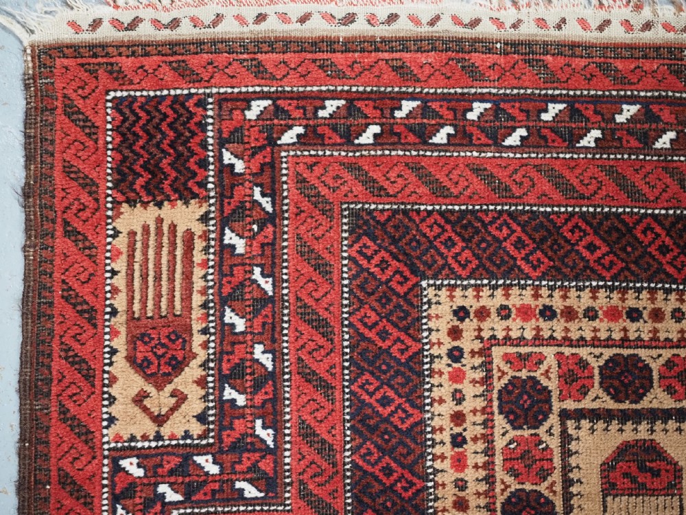 An antique Baluch wool prayer rug featuring a central mihrab arch, tree motifs, hand icons, and geometric borders in dark red, brown, and camel shades. View VI