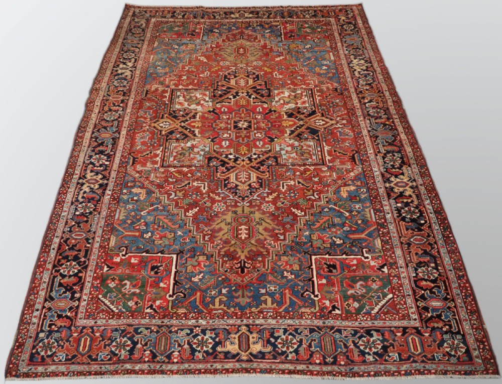 An antique hand-knotted wool Heriz carpet featuring a large central geometric medallion in rust red, navy blue, and cream surrounded by detailed geometric borders.