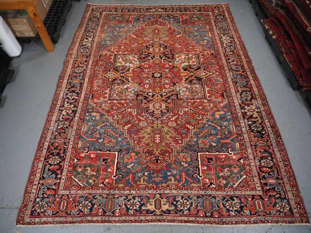 An antique hand-knotted wool Heriz carpet featuring a large central geometric medallion in rust red, navy blue, and cream surrounded by detailed geometric borders. View III