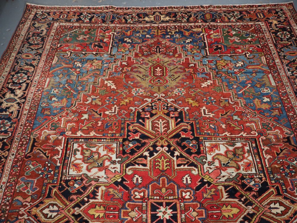 An antique hand-knotted wool Heriz carpet featuring a large central geometric medallion in rust red, navy blue, and cream surrounded by detailed geometric borders. View IV