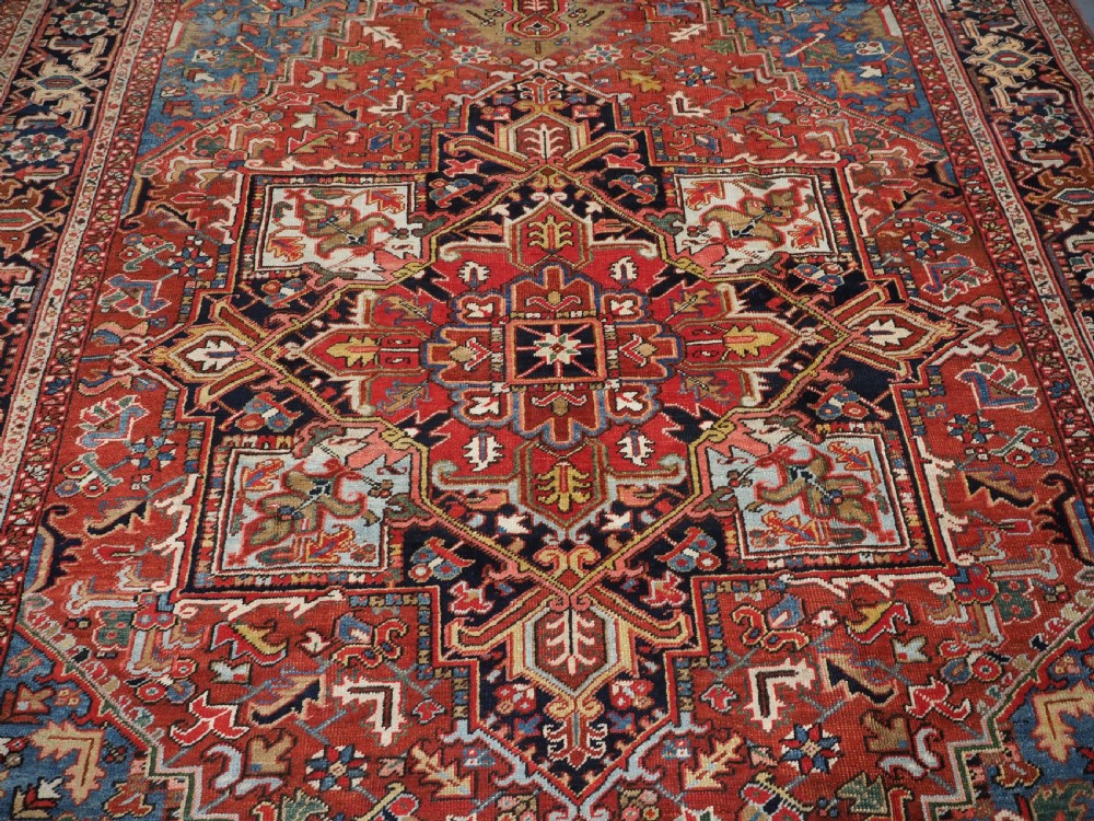 An antique hand-knotted wool Heriz carpet featuring a large central geometric medallion in rust red, navy blue, and cream surrounded by detailed geometric borders. View V