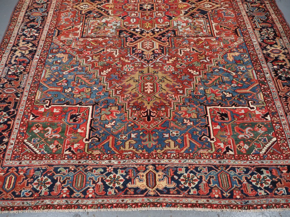 An antique hand-knotted wool Heriz carpet featuring a large central geometric medallion in rust red, navy blue, and cream surrounded by detailed geometric borders. View VI