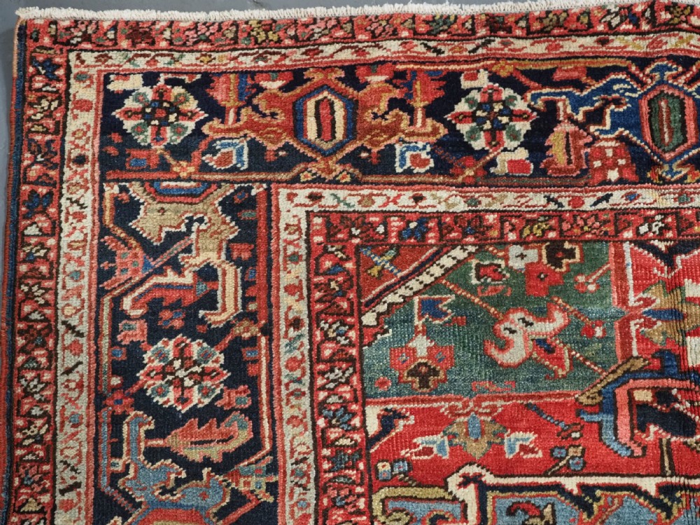 An antique hand-knotted wool Heriz carpet featuring a large central geometric medallion in rust red, navy blue, and cream surrounded by detailed geometric borders. View VII