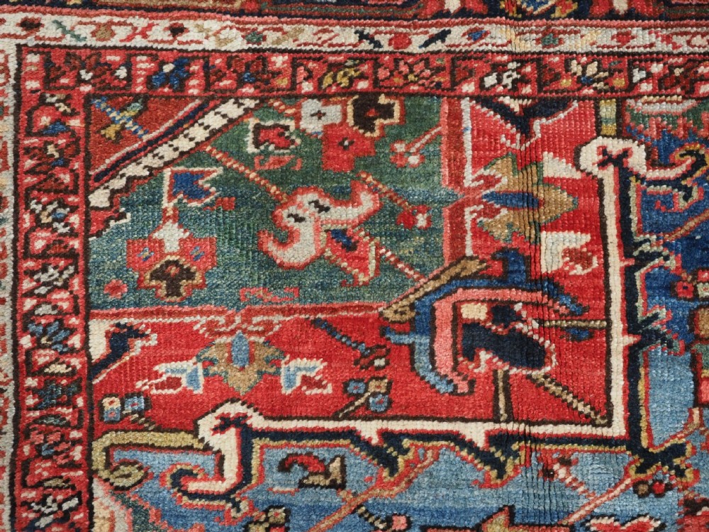 An antique hand-knotted wool Heriz carpet featuring a large central geometric medallion in rust red, navy blue, and cream surrounded by detailed geometric borders. View IX