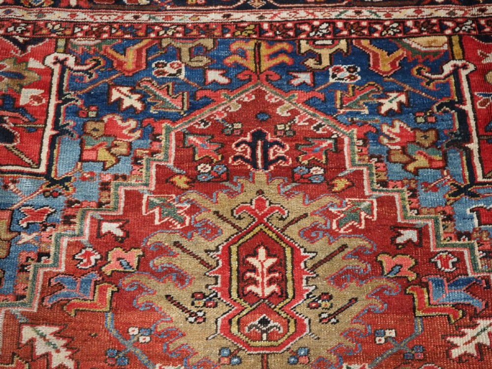 An antique hand-knotted wool Heriz carpet featuring a large central geometric medallion in rust red, navy blue, and cream surrounded by detailed geometric borders. View X