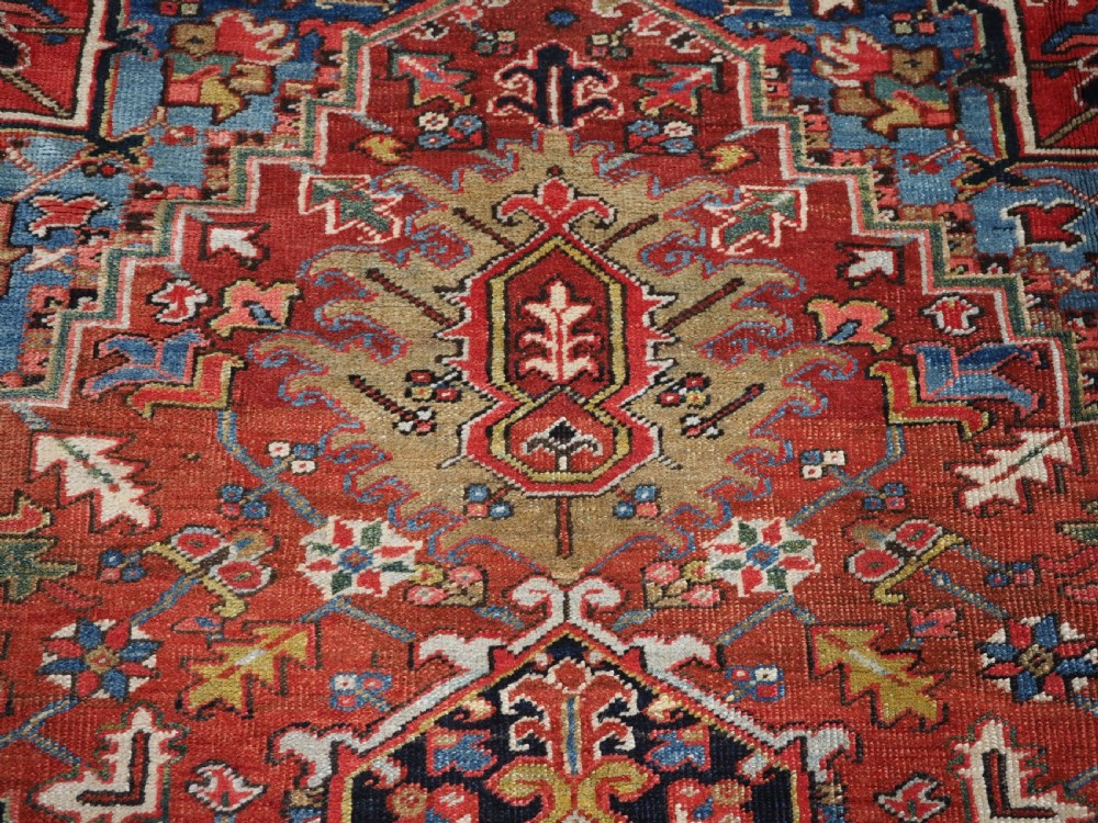 An antique hand-knotted wool Heriz carpet featuring a large central geometric medallion in rust red, navy blue, and cream surrounded by detailed geometric borders. View XI